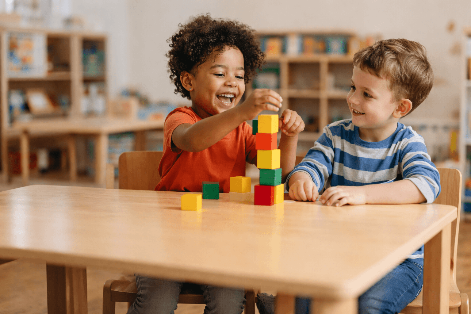 Two preschool children smiling and building with colorful blocks.